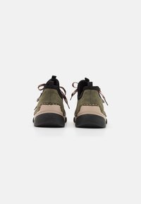 Chaussures en daim vert avec une semelle beige clair, des accents noirs et des lacets texturés, présentant un design à profile bas et un dos arrondi.