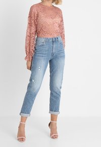 Lyserød blonde top med lange ærmer og rund halsudskæring, parret med lyseblå højtaljede slidte jeans. Modellen har strappy lyserøde stiletter på.