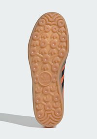 Talpa de sneaker din cauciuc, texturată cu modele circulare și ondulate, având o schemă de culori portocalie și neagră și un detaliu cu un logo circular.
