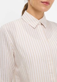 Light striped shirt made of textured fabric; features a classic collar and front buttons, with vertical beige and cream stripes.