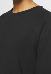 Sweatshirt noir à col rond, fabriqué en tissu doux. Comporte des manches raglan et une couture texturée au niveau de l'encolure et des coutures.