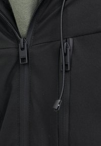 Sort zip-jakke med to forreste lynlåse, justerbar snor og en glat struktur med mat finish. Underskjold synligt.