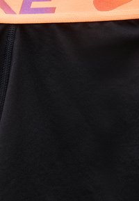 Close-up van zwart en roze stof met zwarte naadstiksels, waarbij de textuur en contrasterende kleuren van de kledingstof zichtbaar zijn.