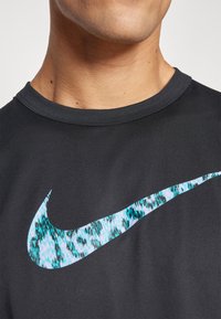 Svart trenings t-skjorte med rund hals, prydet med en stor, flerfarget Nike swoosh-logo i blått og hvitt digitalt mønster.