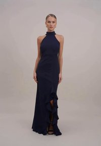 Abito halter neck blu navy con corpino aderente e orlo arricciato. Presenta uno spacco alto e una texture liscia, creando una silhouette elegante.