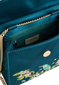 Modra torbica z zlatim verižnim trakami, s cvetličnim vezenjem, magnetno zapiranje in notranjim žepom z zadrgo, izdelana iz gladkega blaga.