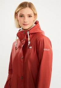 Chaqueta impermeable roja con capucha, que presenta cordones ajustables, bordado del logo y cierres de botón. Textura suave y diseño estructurado.