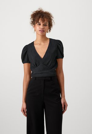 Black textured top with a deep V-neck and puff sleeves, paired with high-waisted black trousers. Smooth fabric with a fitted waist.