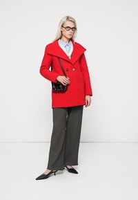 Red wool peacoat with a wide collar and double-breasted buttons, paired with gray wide-leg trousers and black pointed-toe shoes.