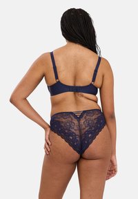 Ensemble de lingerie en dentelle bleu marine comprenant un soutien-gorge à bretelles réglables et un string assorti avec des motifs floraux et des détails de lien à l'arrière.