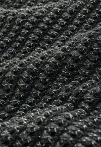 Tissu noir texturé avec un motif en tricot, présentant un mélange de fibres douces et de subtils accents brillants tissés tout au long.