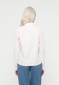 Camicia a righe rosa chiaro con maniche lunghe e colletto, vista dal retro. Abbinata a jeans di denim blu chiaro.