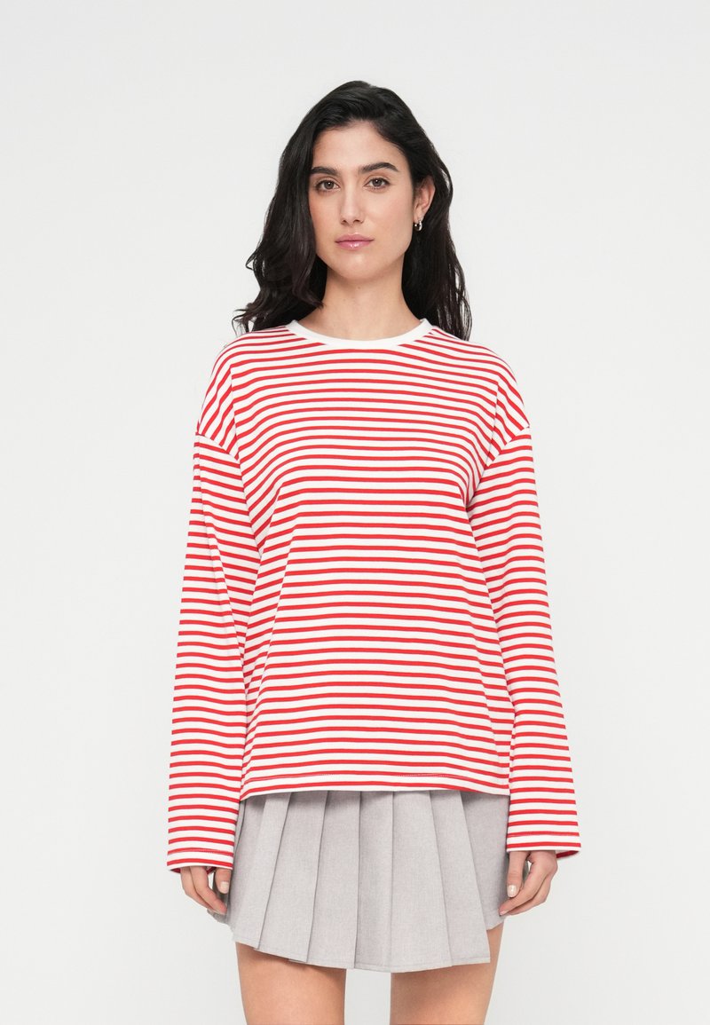 Κόκκινη και λευκή ριγέ μπλούζα με μακριά μανίκια και στρογγυλή λαιμόκοψη, συνδυασμένη με πλισέ γκρι φούστα, κατασκευασμένη από μαλακό, αεριζόμενο ύφασμα.