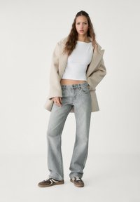 Manteau en boucle beige sur un haut blanc ajust�é et un jean large gris clair, associé à des baskets marron avec des rayures blanches et des lacets noirs.