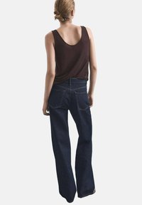 Jeans évasés en denim bleu foncé avec poches arrière, associés à un débardeur ajusté marron. Le tissu semble lisse et légèrement extensible.