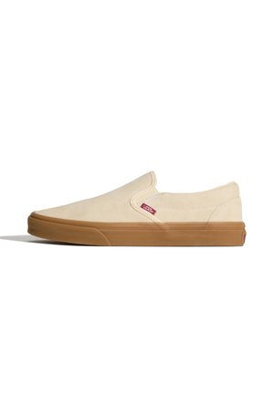 Beige slip-on Vans sneaker med brun gummisål og lille rød Vans logo tag nær den elastiske sidepanel.
