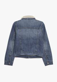 Džínová bunda v středně modré barvě s měkkým krémově zbarveným límcem z umělé kožešiny, zapínáním na knoflíky na manžetách a krátkým střihem. Má vybledlou texturu.