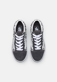 Musta-valkoiset Vans-tennarit, joissa on valkoiset nauhat ja leopardikuosiset sivut, näkymä ylhäältä valkoista taustaa vasten.