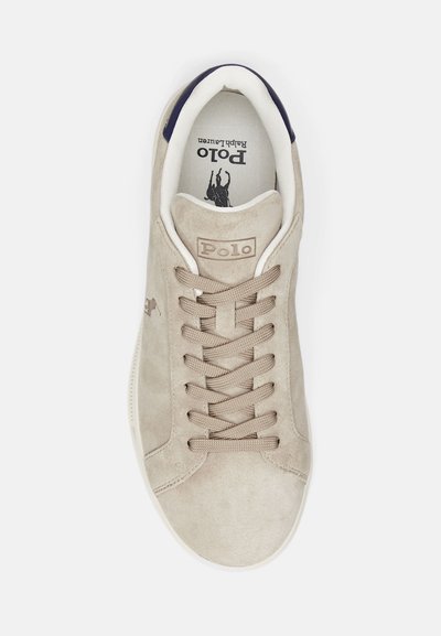 Beige suede sneaker featuring a white sole, round toe, and a lace-up front with a "Polo" logo and a textured tan accent.