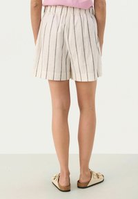 White linen shorts with vertical dark stripes, elastic waistband, and side pockets. Paired with beige slip-on sandals.