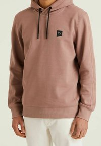 Felpa con cappuccio di colore rosa polveroso, realizzata in tessuto morbido, con un patch logo nero, cordini regolabili e polsini e orlo ribattuti.