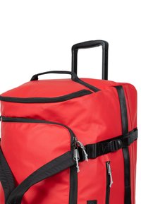 Red duffel bag with black accents, featuring top handle, retractable handle, and multiple zippered pockets. Made of durable fabric.