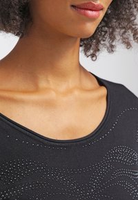 Top nero con scollatura ampia, caratterizzato da un motivo testurizzato di strass disposti in disegni ondulati sulla parte anteriore. Tessuto dalla texture liscia.