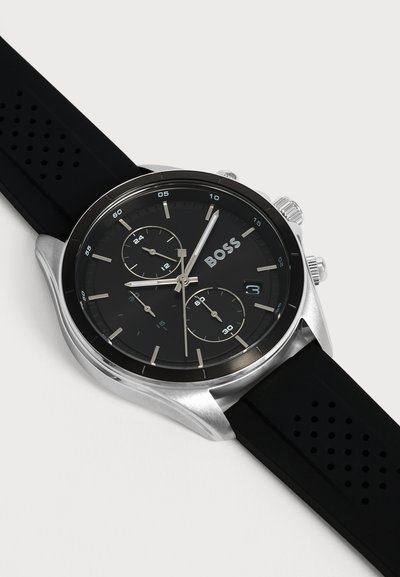 Montre chronographe noire avec boîtier argenté, bracelet noir perforé, trois sous-cadrans et fenêtre de date, marquée BOSS sur le cadran.