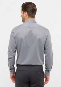 Grijs patroon shirt met lange mouwen, knoopmanchetten en een klassieke kraag. De stof heeft een klein geometrisch ontwerp. Gecombineerd met donkere broek.