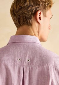 Heled roosa lühikeste varrukatega särk klassikalise kraega ja selja voldiga. Omab kahte metallist kinnitust voldi kohal ventilatsiooni jaoks.