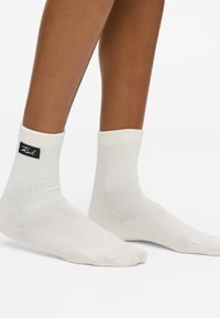 Białe, bawełniane skarpetki za kostkę z prążkowaną fakturą i czarną metką z nazwą marki. Wysokość do kostki z bezszwowym czubkiem.