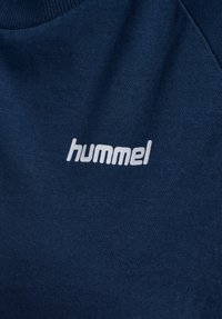 Sweat-shirt bleu marine en tissu doux avec un col rond. Présente un logo "hummel" blanc imprimé sur la poitrine.