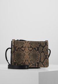 Borsa con motivo in pelle di serpente con una tracolla nera, posata su una superficie bianca contro uno sfondo grigio chiaro.
