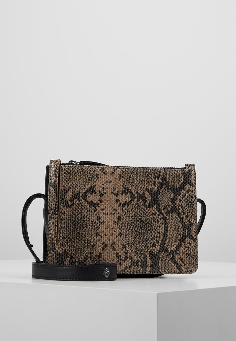 Borsa con motivo in pelle di serpente con una tracolla nera, posata su una superficie bianca contro uno sfondo grigio chiaro.