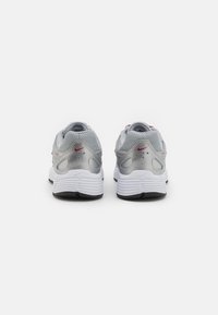 Nike sneakers in silver and white, featuring textured mesh fabric, visible air cushioning, and a small red logo on the heel.