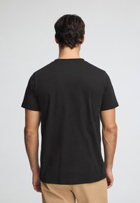 Svart bomulls-t-shirt med rund halsringning och korta ärmar, med en enkel design och en bekväm, avslappnad passform sedd bakifrån.