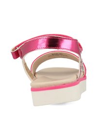 Roze metalen sandaal met een witte plateauzool. Heeft een achterband en een gladde beige voetbed. Dunne bandjes kronkelen rond de enkel.