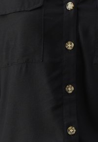 Black button-up shirt featuring gold-tone buttons, two chest pockets, and a smooth, woven texture. The design includes a collar and front placket.