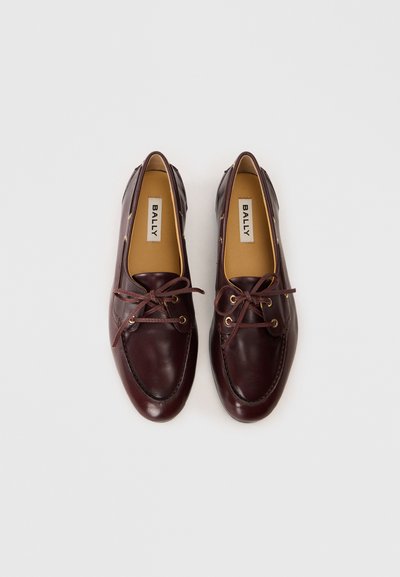 Pantofi loafers din piele burgundy cu vârf rotunjit, șireturi și gromete cu ton auriu. Interiorul are un căptușeală bej cu eticheta mărcii.