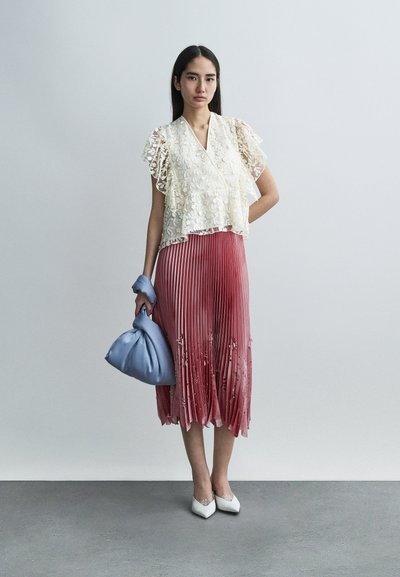 Haut en dentelle avec manches volantées sur une jupe plissée à dégradé rose. Accessoirisé d'un sac à main bleu et de chaussures blanches à bout pointu.