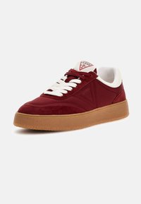 Red and white sneaker with suede and textile materials. Features a gum sole, white laces, and triangular logo on the tongue.
