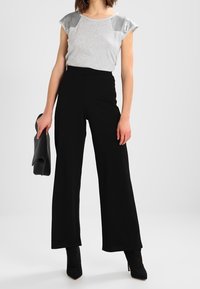 Grå topp med kort ärm och metalliska detaljer, kombinerad med högmidjade svarta vida byxor och svarta spetsiga klackskor.