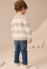 Hellgrau und cremefarbene gestreifte Kabelstrickjacke mit Rundhalsausschnitt, kombiniert mit dunkelblauen Jeans und beigen Sneakers.