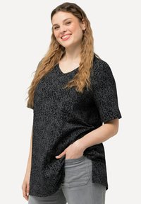 Top negro de manga corta y escote en V, con un patrón floral texturizado. El diseño es holgado, con un dobladillo curvado y bolsillos laterales.