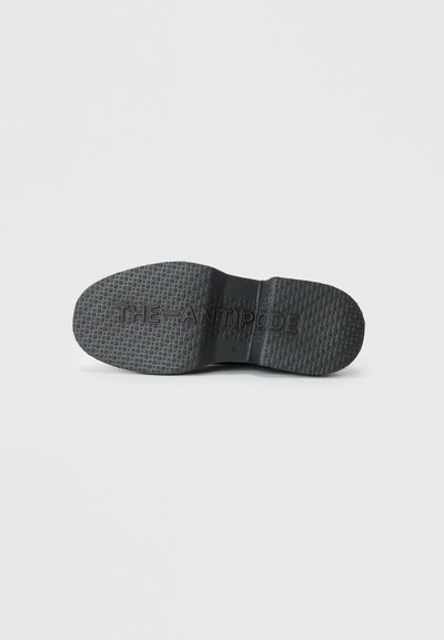 Black rubber shoe sole with textured grip pattern. Inscribed branding "THE ANTIPODE" near the heel. Rounded toe design.
