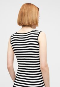 Μαύρο και άσπρο ριγέ, αμάνικο τοπ με ανάγλυφη υφή και στρογγυλή λαιμόκοψη με παράλληλο μοτίβο. Το ύφασμα έχει υφή.