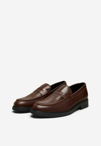 Brown leather loafers with a smooth finish, low heel, and a decorative strap across the upper. The sole is black rubber for traction.