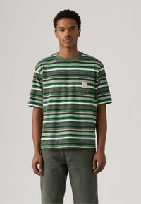 Camiseta de rayas verdes hecha de una tela suave, con rayas horizontales en diferentes tonos de verde y blanco, con un bolsillo en el pecho y cuello redondo.