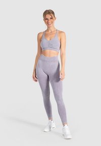 Ljusgrå atletisk crop top med rynkad detalj och matchande leggings. Materialet verkar mjukt och stretchigt; skorna är vita med svarta detaljer.