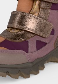 Gros plan d'une chaussure violette et rose avec une semelle texturée et une bride métallique fixée sur le dessus.